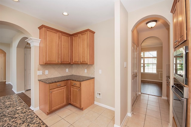 kitchen with appliances with stainless steel finishes, backsplash, light tile patterned floors, and dark stone counters