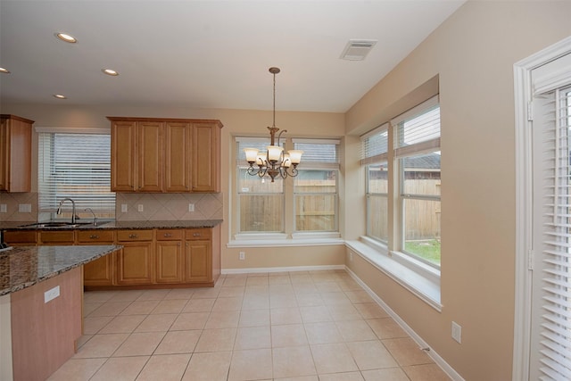 kitchen with dark stone counters, an inviting chandelier, sink, tasteful backsplash, and decorative light fixtures