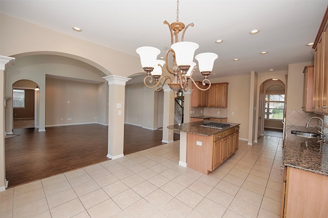 kitchen with sink, tasteful backsplash, a chandelier, dark stone counters, and light tile patterned floors