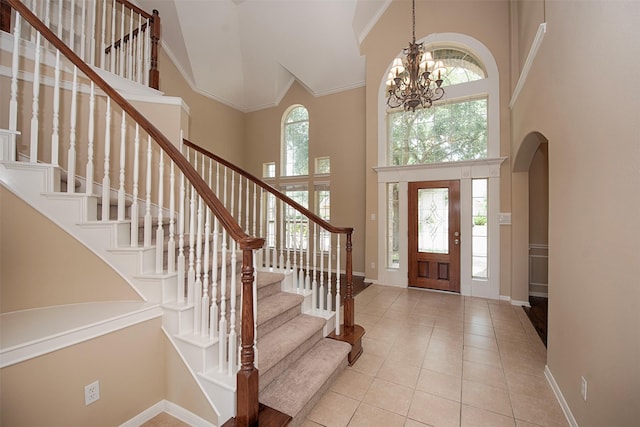 tiled entryway featuring a wealth of natural light, crown molding, a towering ceiling, and an inviting chandelier