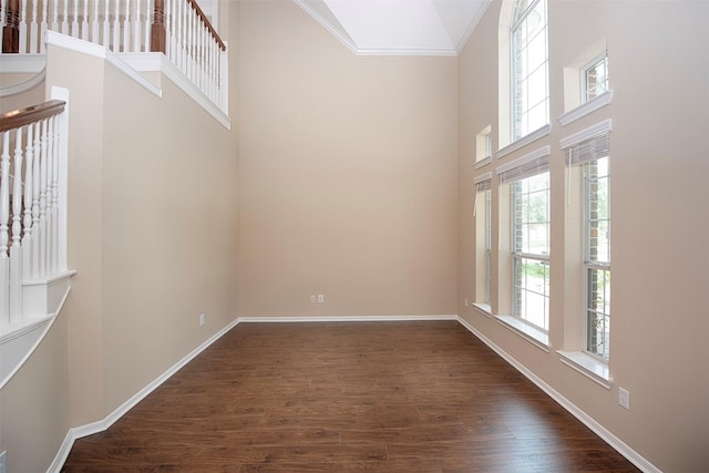 spare room featuring a towering ceiling, crown molding, plenty of natural light, and dark wood-type flooring