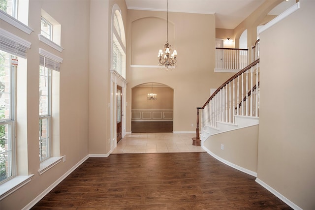 foyer featuring wood-type flooring, ornamental molding, a notable chandelier, and a high ceiling