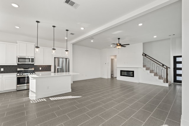 kitchen featuring white cabinetry, visible vents, a kitchen island, stainless steel appliances, and backsplash