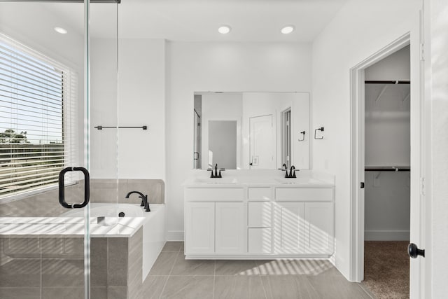 bathroom with a bath, double vanity, a sink, and a spacious closet