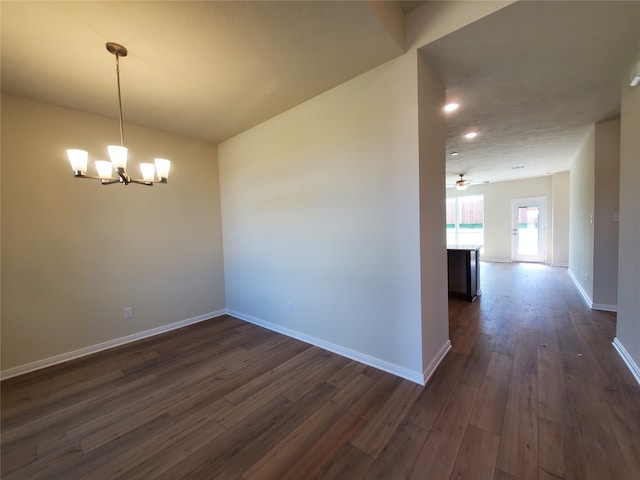 empty room featuring ceiling fan with notable chandelier and dark hardwood / wood-style floors