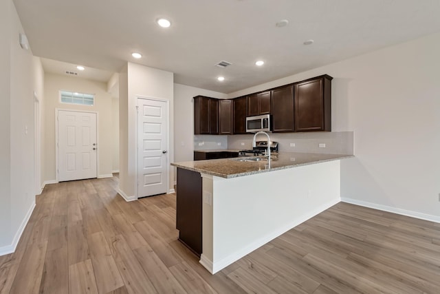 kitchen with stainless steel appliances, light stone countertops, sink, and light hardwood / wood-style flooring