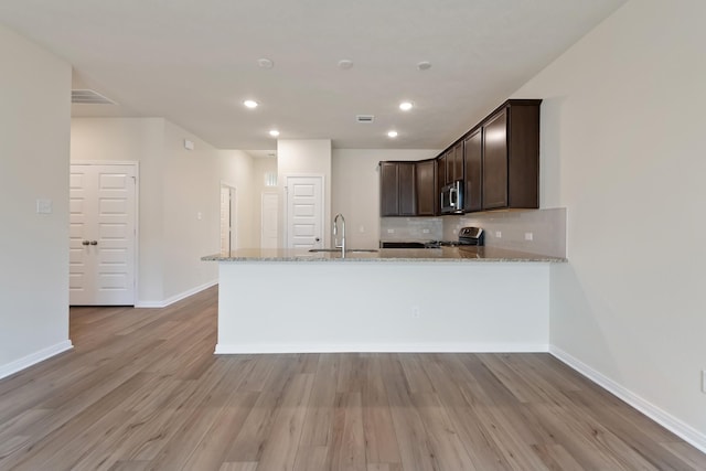 kitchen featuring tasteful backsplash, sink, light stone counters, kitchen peninsula, and stainless steel appliances