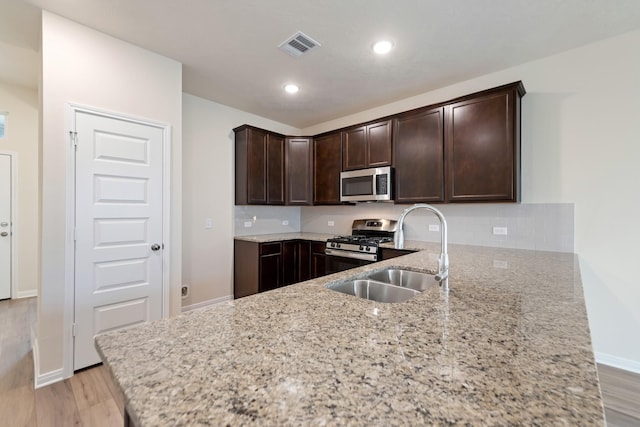 kitchen with sink, light hardwood / wood-style floors, stainless steel appliances, light stone countertops, and dark brown cabinets