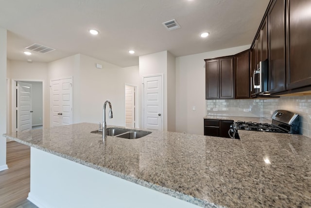 kitchen featuring appliances with stainless steel finishes, tasteful backsplash, sink, dark brown cabinetry, and light stone countertops