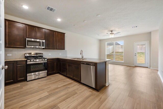 kitchen featuring stainless steel appliances, sink, light hardwood / wood-style floors, and kitchen peninsula