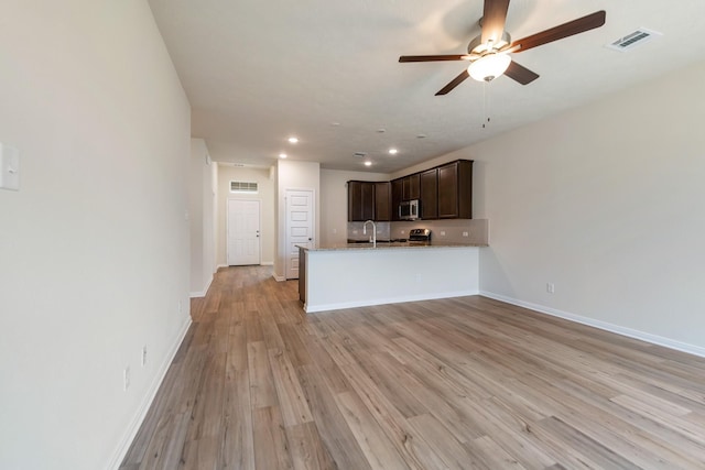 kitchen with kitchen peninsula, ceiling fan, light hardwood / wood-style floors, light stone countertops, and dark brown cabinets