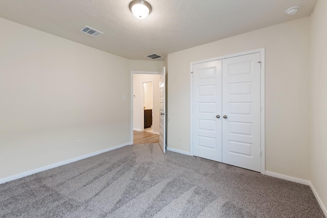 unfurnished bedroom featuring light carpet, a closet, and a textured ceiling