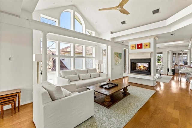 living room featuring ceiling fan, a multi sided fireplace, high vaulted ceiling, and light hardwood / wood-style floors