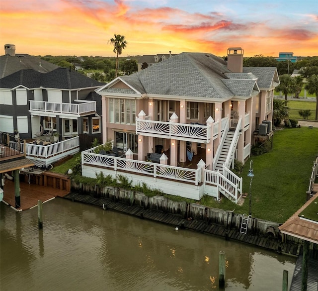 back house at dusk with a balcony, a water view, and central AC