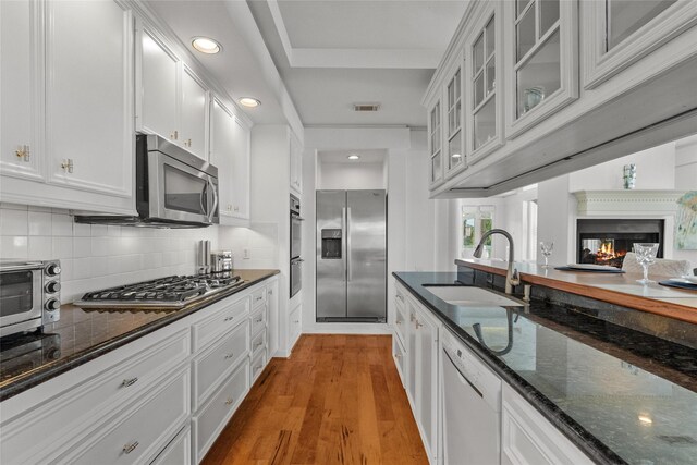 kitchen with stainless steel appliances, backsplash, dark stone counters, white cabinetry, and light hardwood / wood-style flooring