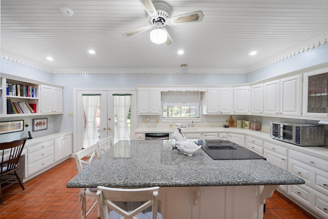 kitchen featuring a kitchen island, stainless steel appliances, dark stone countertops, a kitchen bar, and white cabinets