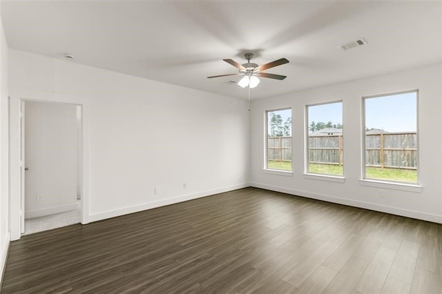 empty room with dark wood-style flooring, visible vents, baseboards, and ceiling fan