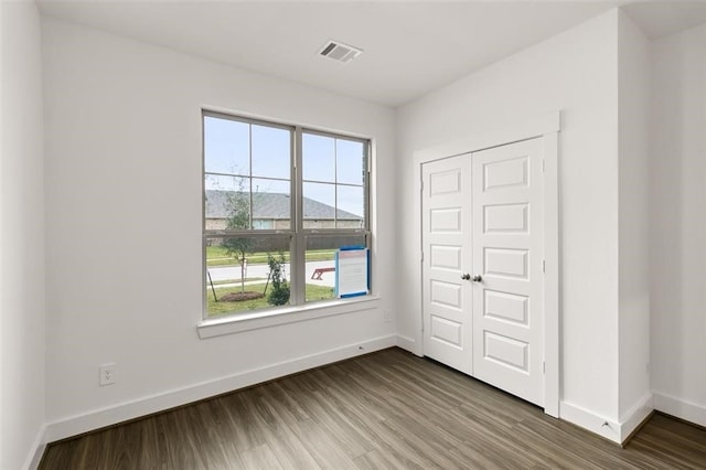 unfurnished bedroom with baseboards, wood finished floors, visible vents, and multiple windows