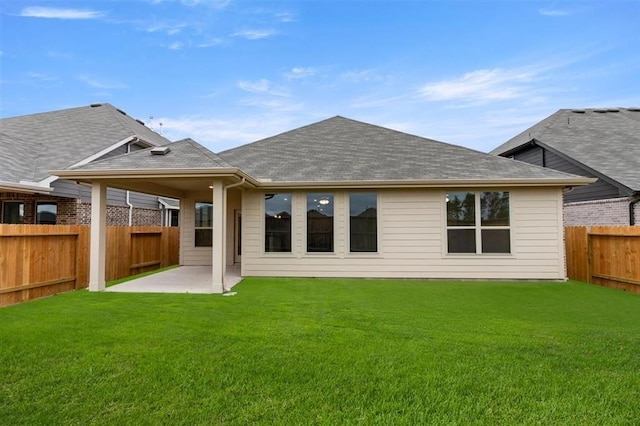 back of house featuring a lawn, a fenced backyard, roof with shingles, and a patio