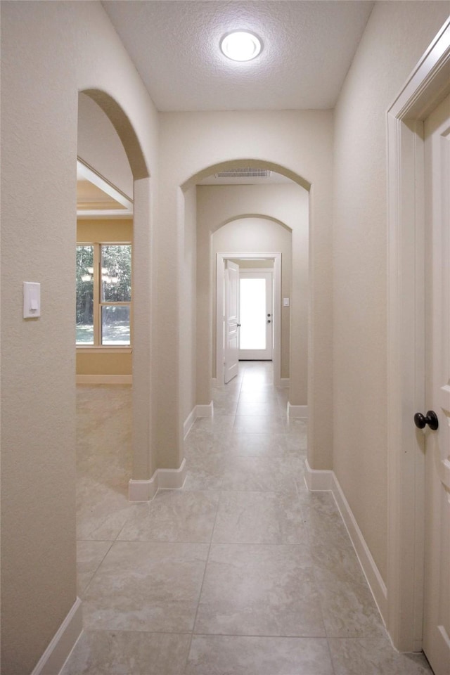 hall with a textured ceiling and light tile floors