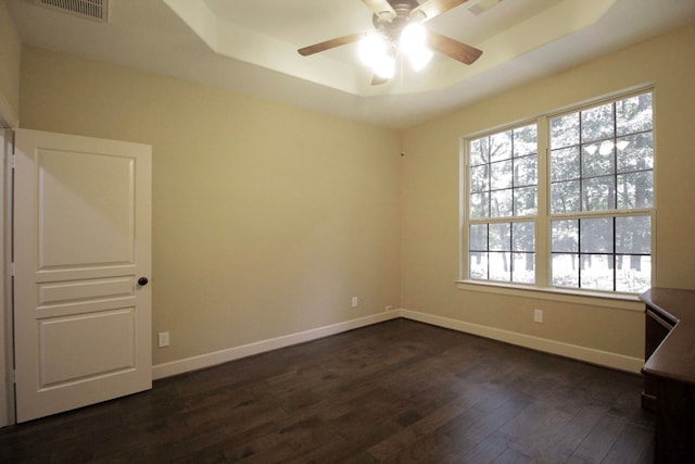 unfurnished room with dark wood-type flooring, plenty of natural light, ceiling fan, and a raised ceiling