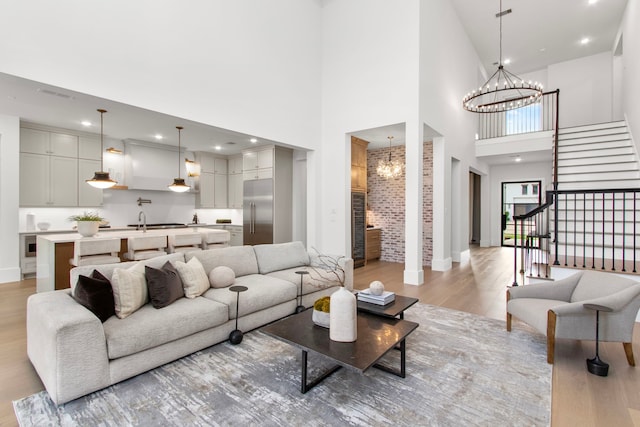 living room featuring an inviting chandelier, sink, a high ceiling, and light hardwood / wood-style flooring