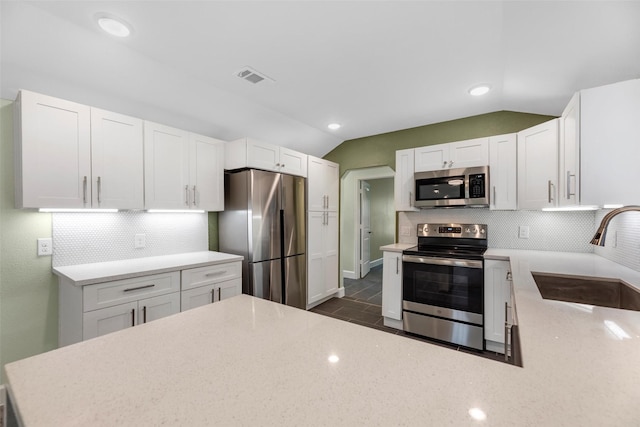 kitchen featuring appliances with stainless steel finishes, tasteful backsplash, white cabinetry, sink, and lofted ceiling