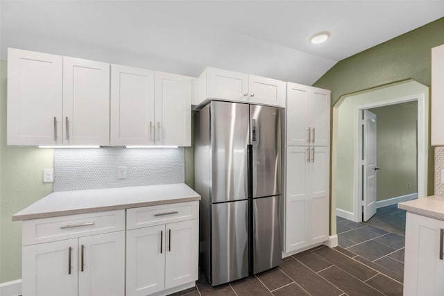 kitchen featuring decorative backsplash, vaulted ceiling, white cabinets, and stainless steel refrigerator