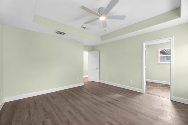 unfurnished bedroom with ceiling fan, a tray ceiling, dark hardwood / wood-style floors, and a walk in closet