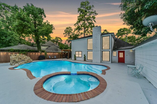 pool at dusk featuring a patio and an in ground hot tub