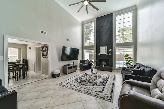 living room with a towering ceiling, ceiling fan, a large fireplace, and light tile floors