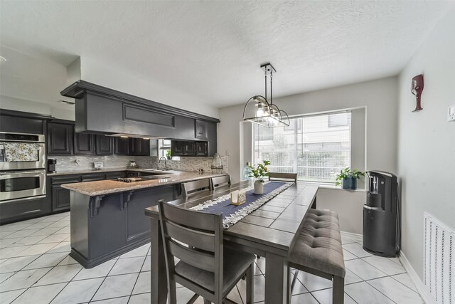 kitchen featuring double oven, hanging light fixtures, tasteful backsplash, sink, and a breakfast bar