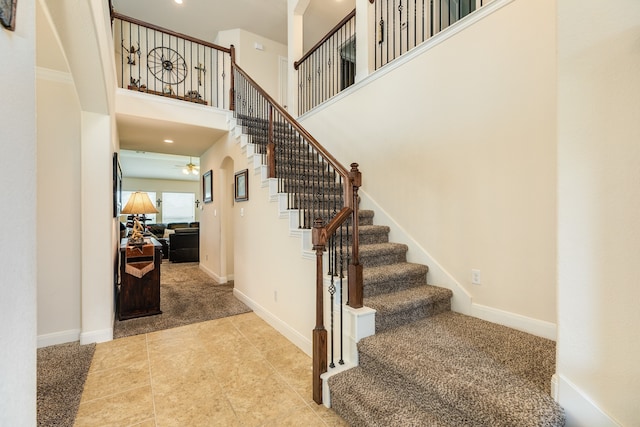 stairs featuring tile floors, ceiling fan, and a high ceiling