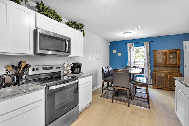 kitchen with stainless steel appliances, light stone countertops, white cabinetry, and light hardwood / wood-style floors