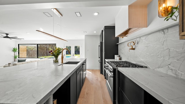 kitchen with light stone countertops, sink, tasteful backsplash, appliances with stainless steel finishes, and light wood-type flooring