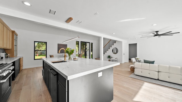 kitchen featuring sink, ceiling fan, an island with sink, light hardwood / wood-style floors, and stainless steel range oven