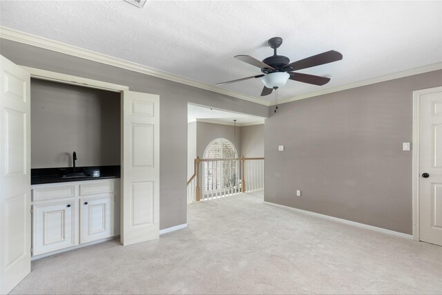 unfurnished living room featuring ceiling fan, crown molding, light carpet, a textured ceiling, and sink