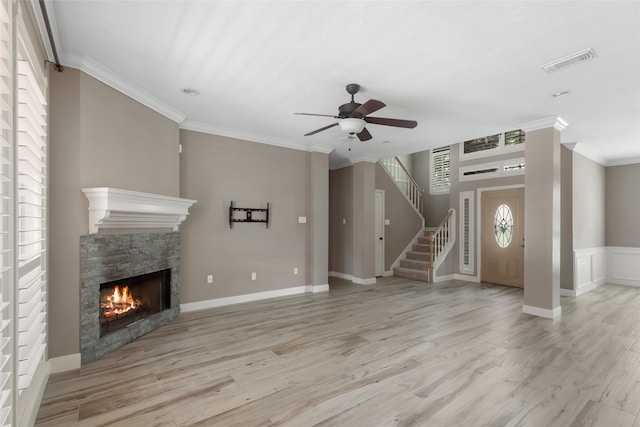 unfurnished living room with a stone fireplace, crown molding, light wood-type flooring, and ceiling fan