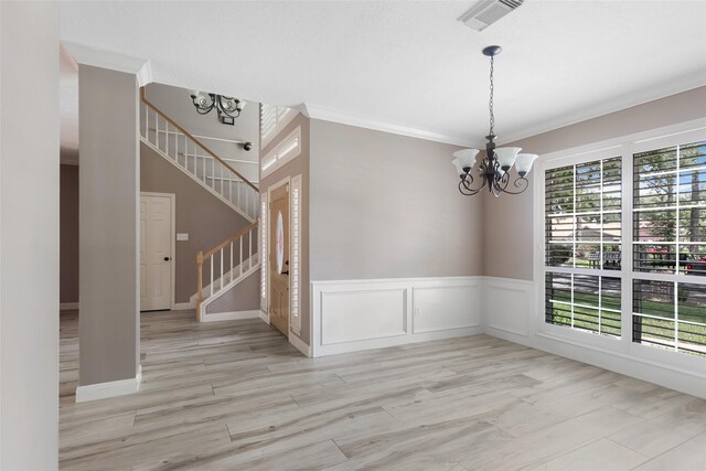 spare room with a notable chandelier, light hardwood / wood-style flooring, crown molding, and a healthy amount of sunlight