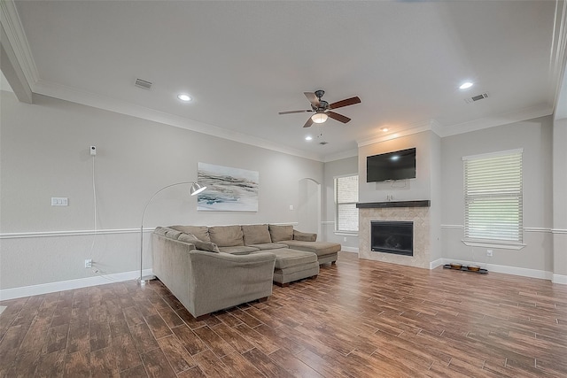 living room featuring wood-type flooring, plenty of natural light, crown molding, and a tiled fireplace