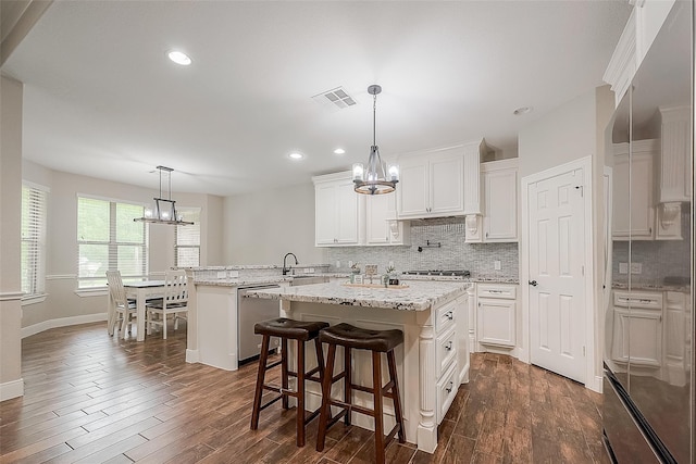 kitchen featuring dark wood-style flooring, stainless steel appliances, visible vents, decorative backsplash, and an inviting chandelier