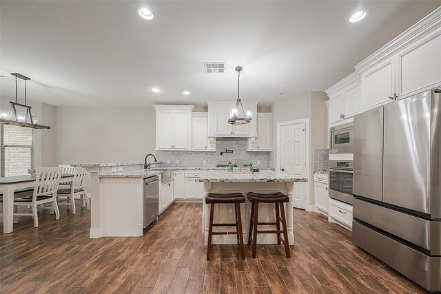 kitchen with white cabinets, pendant lighting, stainless steel appliances, and dark wood-type flooring