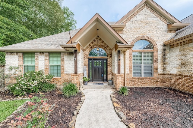 doorway to property featuring stone siding, a shingled roof, and brick siding