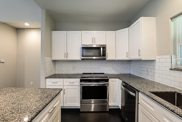 kitchen with white cabinets, backsplash, appliances with stainless steel finishes, and dark stone countertops