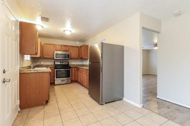 kitchen featuring light stone countertops, ceiling fan, sink, stainless steel appliances, and light tile patterned floors