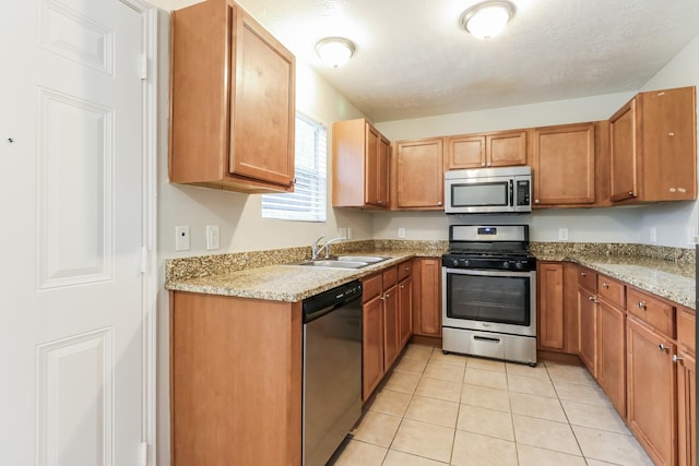 kitchen with light tile patterned floors, light stone countertops, sink, and appliances with stainless steel finishes