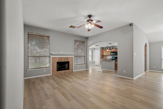 unfurnished living room with arched walkways, visible vents, light wood finished floors, and a tile fireplace