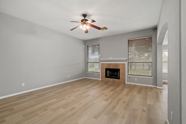 unfurnished living room with baseboards, a tile fireplace, a ceiling fan, and light wood-style floors