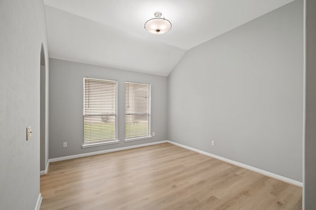 spare room featuring light wood-type flooring, lofted ceiling, and baseboards