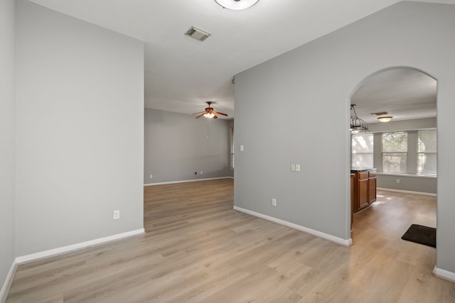 empty room with arched walkways, light wood-style flooring, visible vents, and baseboards